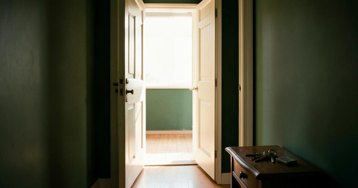Porte d'entrée ouverte laissant entrer la lumière du jour dans un couloir sombre, clés posées sur une console