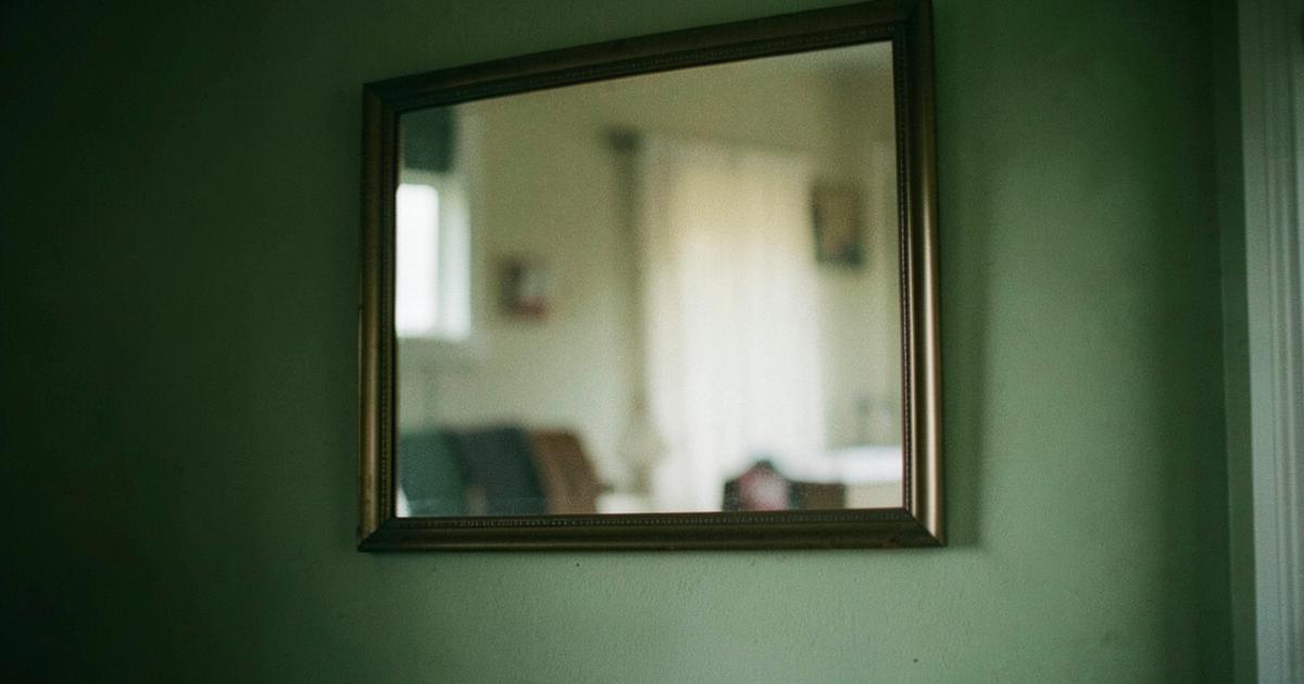 Miroir ancien accroché à un mur vert, reflétant une pièce floue et indistincte