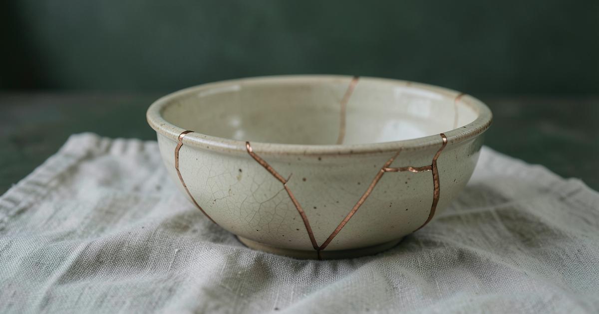 Bol en céramique fêlé et recollé avec des veines de bronze, posé sur un lin froissé