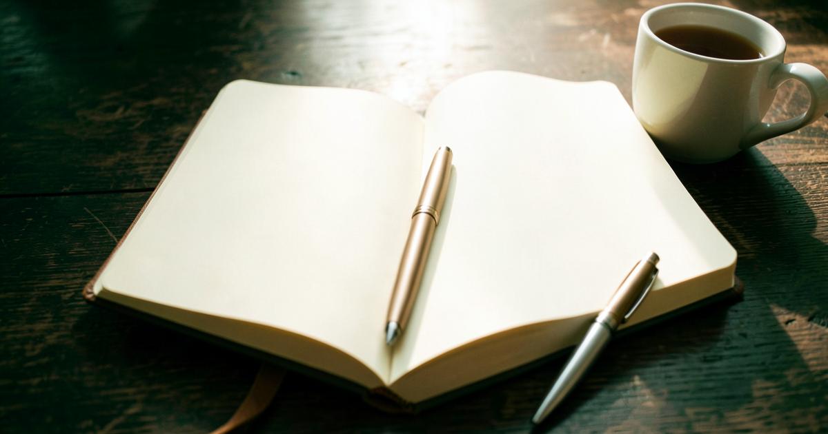 Carnet ouvert aux pages vierges, stylo et tasse de thé sur une table en bois sombre